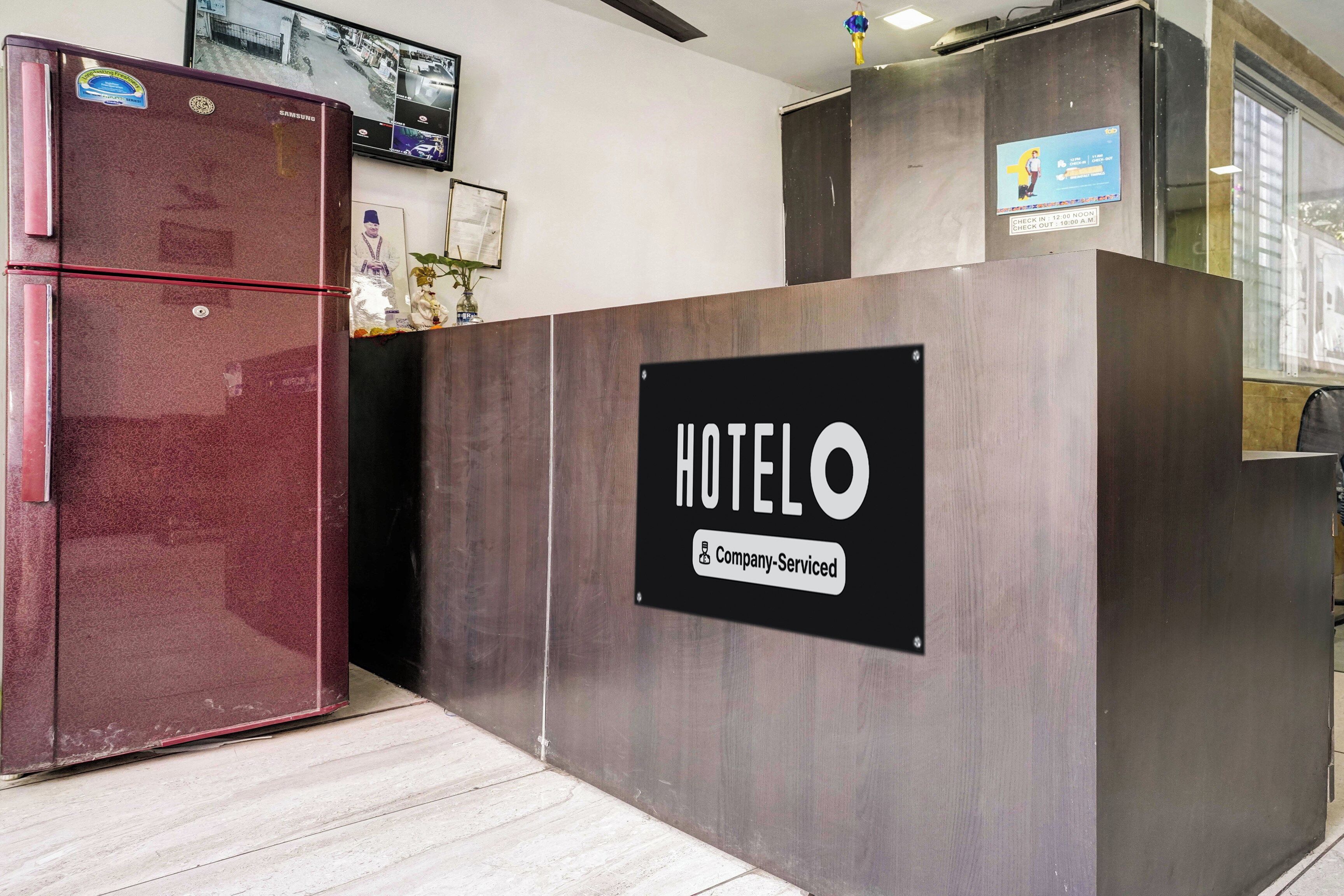 En hotelfacade med reception, et skilt der siger 'HOTEL O', et Samsung-køleskab og et overvågningskamera.