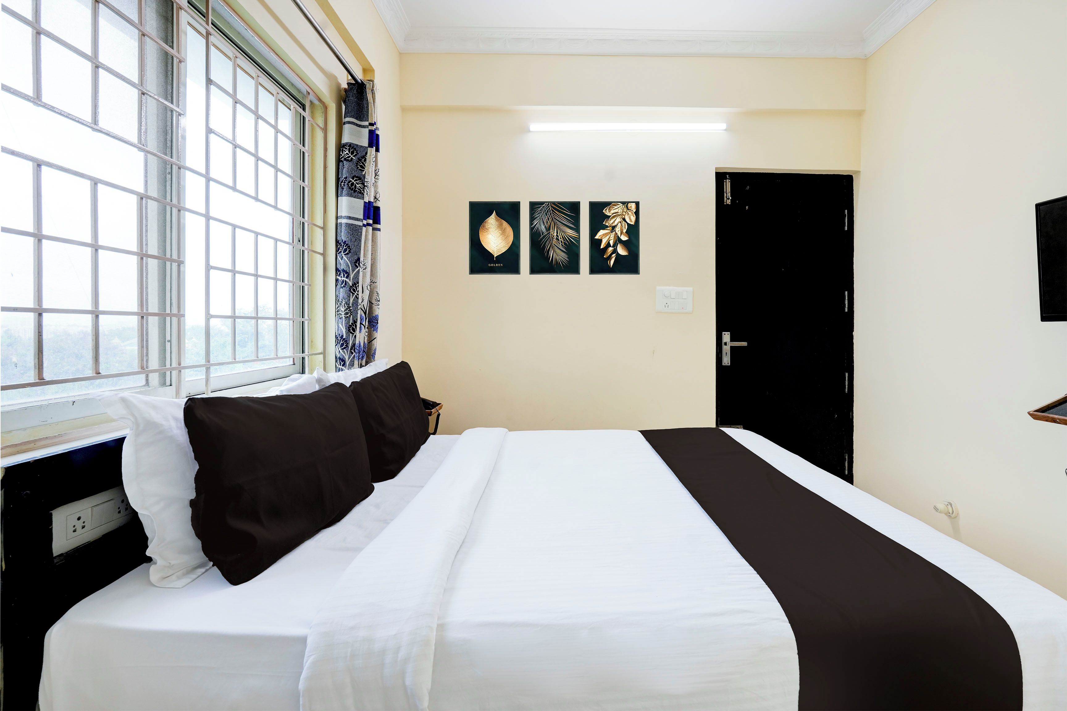 Habitación de hotel con cama, ventana con vistas y obras de arte en la pared.