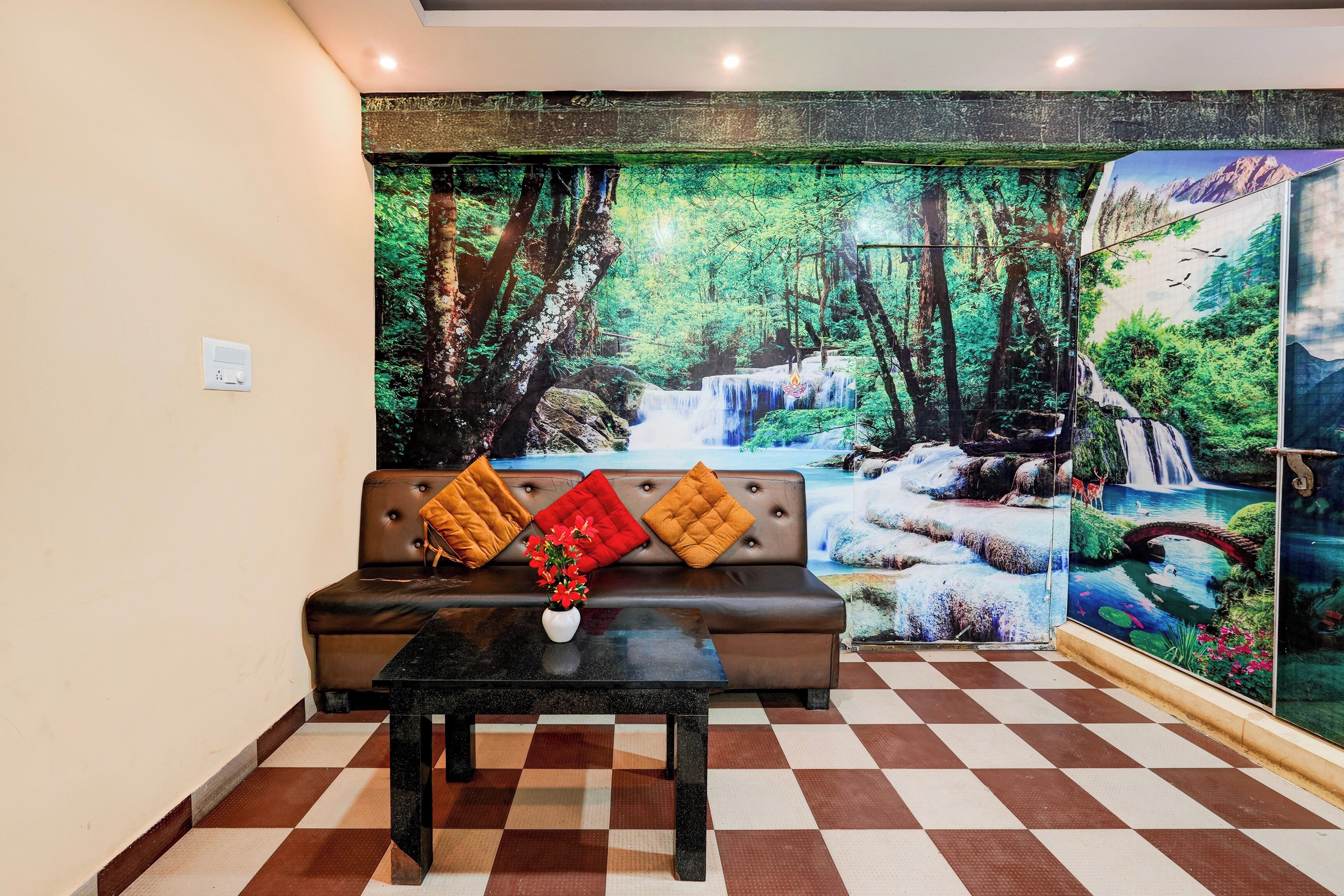A room with a checkered floor, a sofa with cushions, a table with a vase, and a large forest mural on the wall.