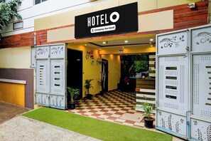 Entrada de hotel com chão xadrez, placa indicando serviço corporativo e aviso.