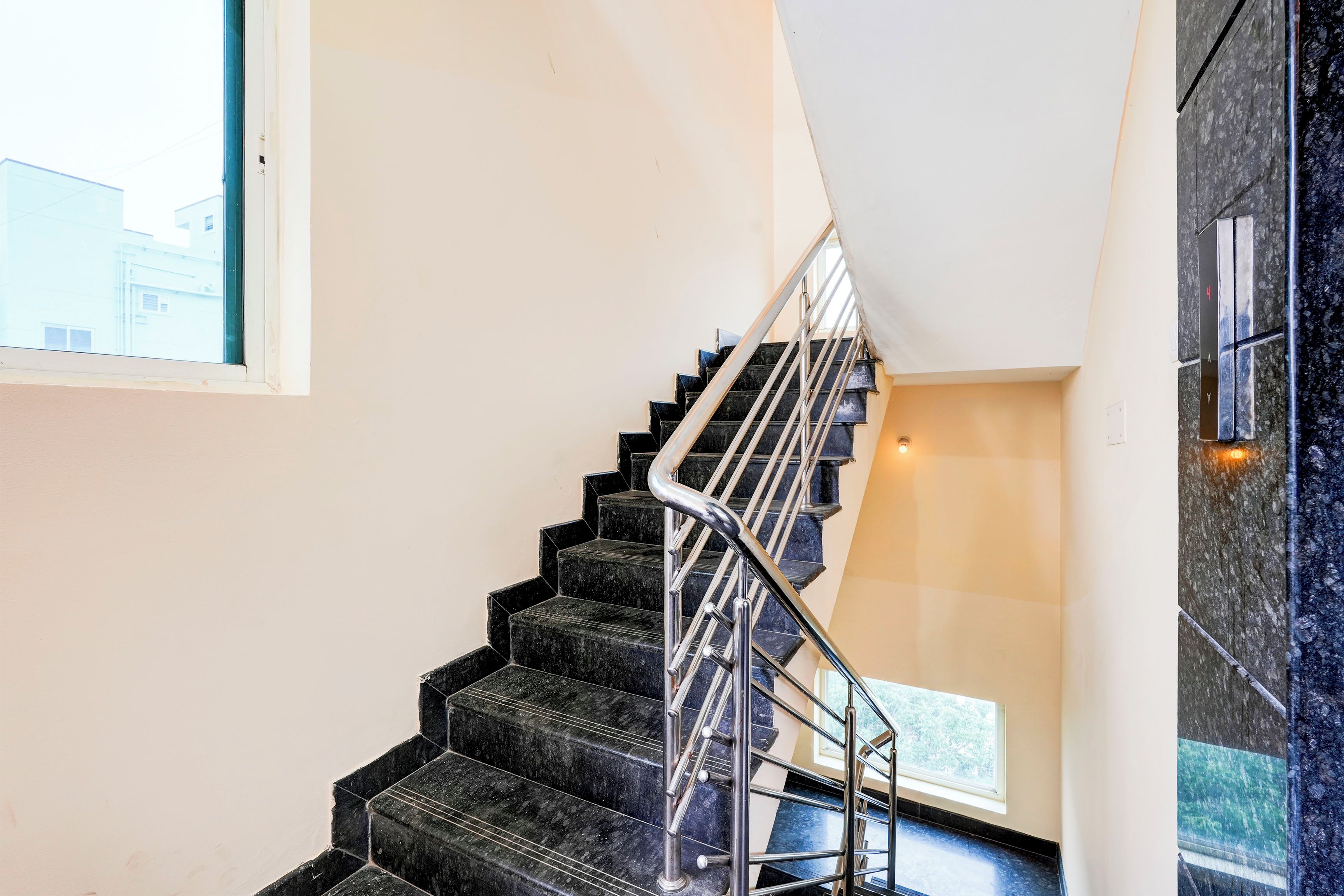 A modern staircase with black steps and a metal railing, leading to a landing with a window.