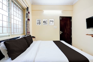 Ein Hotelzimmer mit einem Bett, einem Vorhangfenster, einer Tür und einem an der Wand montierten Fernseher.