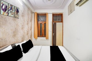 Una habitación de hotel con una cama, un ventanal con cortinas, una puerta y una pared con un cuadro floral.