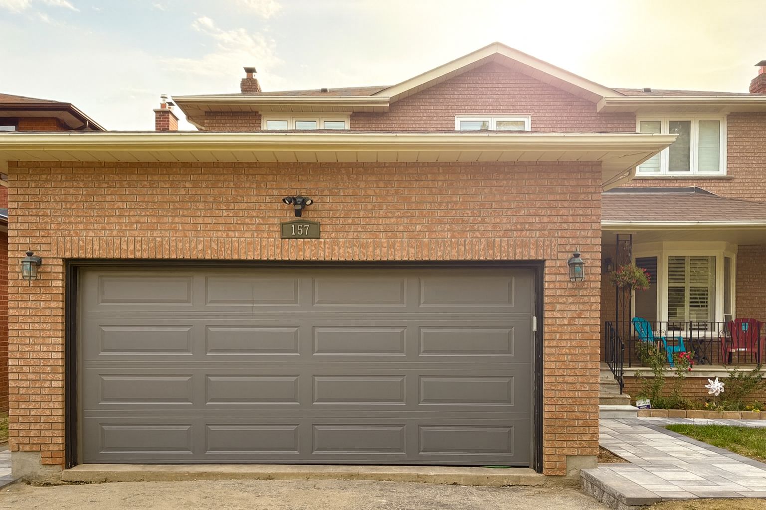 A residential garage with a brick facade, a garage door, and a house number 157.