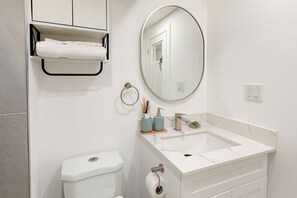 A bathroom with a toilet, sink, mirror, towel rack, and a small shelf with toiletries. - Cozy apartment w/1 Bedroom+ Sofa bed, Parking, near Airport/427/Mall/Market (Toronto)