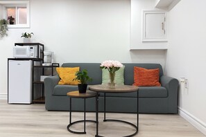 A modern living room with a grey sofa, a small round table, and a potted plant. - Cozy apartment w/1 Bedroom+ Sofa bed, Parking, near Airport/427/Mall/Market (Toronto)