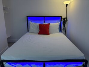 A bed with white bedding and a red pillow, a black metal headboard, and a wall-mounted lamp. - Cozy apartment w/1 Bedroom+ Sofa bed, Parking, near Airport/427/Mall/Market (Toronto)