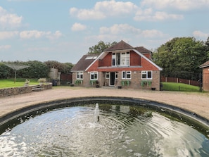 A two-story house with a brick facade, a front garden, and a small pond in the foreground. - Panel Place (Hastings)