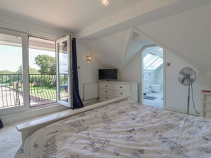 A bedroom with a large bed, a TV, a fan, and a view of a garden through a sliding door. - Panel Place (Hastings)