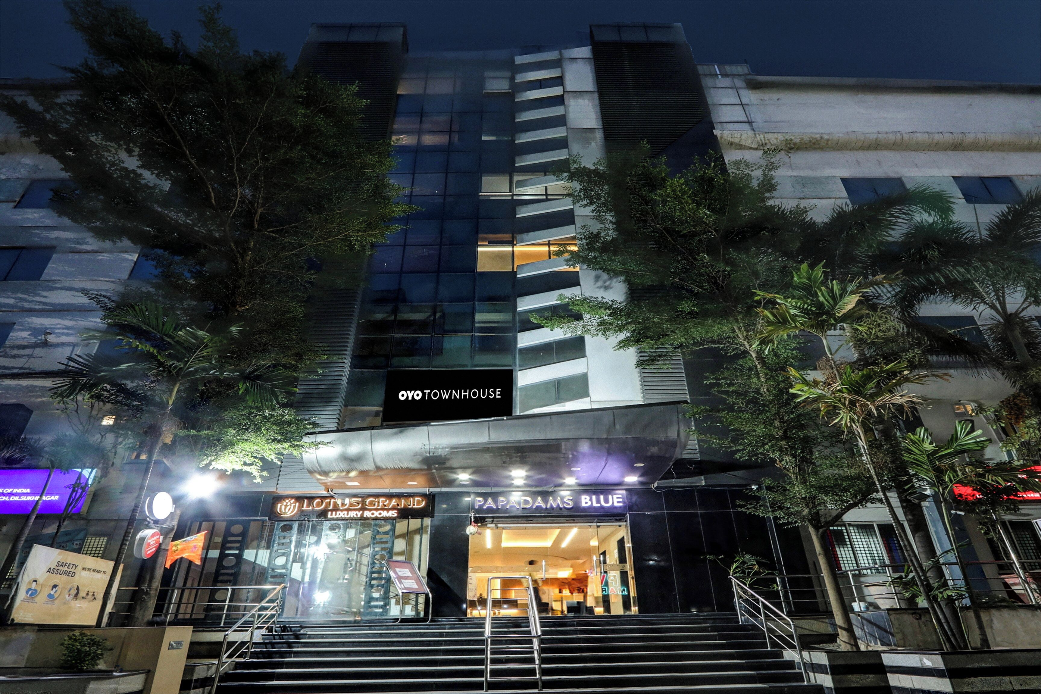 A multi-story building with a prominent entrance, a sign for 'OYO TOWNHOUSE,' and a visible 'LOTUS GRAND LUXURY ROOMS' sign.