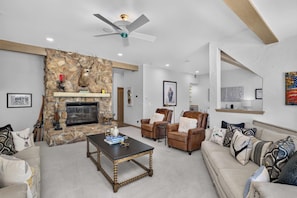 A living room with a stone fireplace, leather sofas, a coffee table, and a ceiling fan. - Alpine Haus Game Room & Views (Avon)