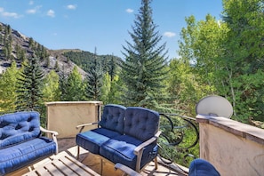 An outdoor seating area with two blue cushioned chairs and a bench, overlooking a mountainous landscape with dense forest. - Alpine Haus Game Room & Views (Avon)