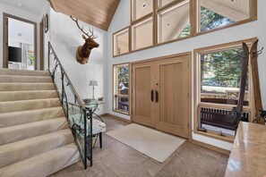 A staircase with a glass railing, a mounted deer head, and a wooden door with a window. - Alpine Haus Game Room & Views (Avon)