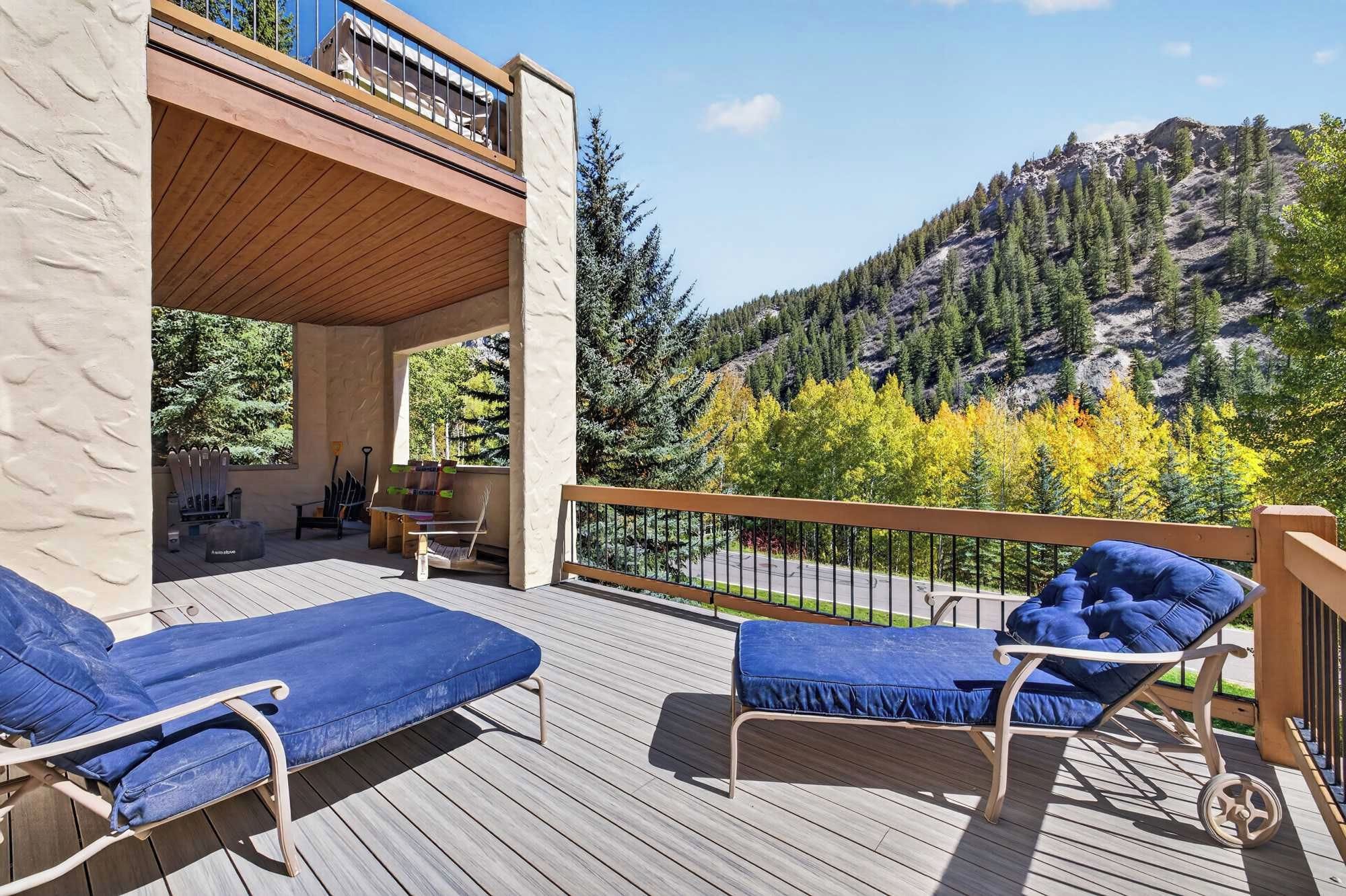 A deck with two blue lounge chairs, a wooden railing, and a view of a forested mountain.