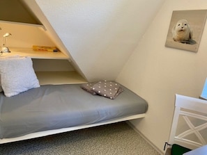 A small, triangular room with a bed, a pillow, a lamp, and a framed picture on the wall. - Holiday Apartment in Wyk on Fohr With Wi-fi (Wyk auf Foehr)