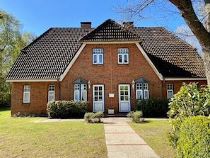 Ein zweistöckiges Backsteinhaus mit einer symmetrischen Fassade, einem zentralen Eingangsbereich und einer kleinen Veranda.