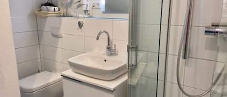 Een badkamer met een wit wastafelmeubel, toilet en een douchecabine met glazen wanden.