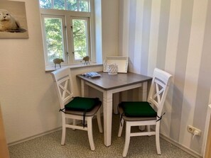 Ein kleiner Essbereich mit Tisch und zwei Stühlen, ein Fenster mit Blick auf Bäume und ein dekoratives Element an der Wand.