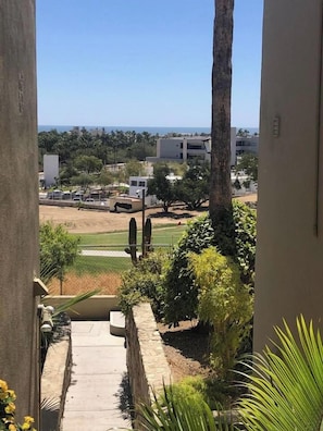 A view from a balcony overlooking a landscaped area with a pathway, palm trees, and distant buildings. - Ocean and Golf Views | Walk to Beach & Downtown (San Jose Del Cabo)