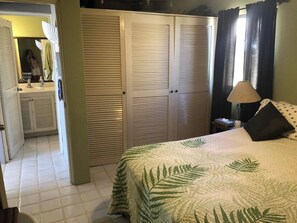 A bedroom with a bed, a nightstand, a lamp, a closet, and a bathroom visible through an open door. - Ocean and Golf Views | Walk to Beach & Downtown (San Jose Del Cabo)