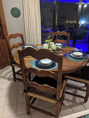 A dining table with four chairs, a vase with flowers, and a view of the city at night. - Ocean and Golf Views | Walk to Beach & Downtown (San Jose Del Cabo)