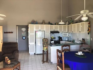 A compact kitchen with white cabinets, a dining area with a blue tablecloth, and a ceiling fan. - Ocean and Golf Views | Walk to Beach & Downtown (San Jose Del Cabo)