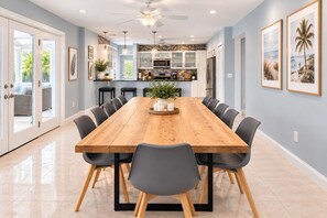A spacious dining area with a long wooden table, surrounded by chairs, in a modern kitchen with white cabinets and a stone backsplash. - Ultimate Escape | Epic Game Room, Pool, Sleeps 16+ (Longwood)