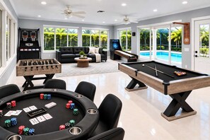 A pool table, foosball table, and blackjack table in a well-lit room with large windows and a view of a pool outside. - Ultimate Escape | Epic Game Room, Pool, Sleeps 16+ (Longwood)