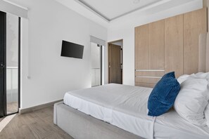 A modern bedroom with a bed, a television mounted on the wall, and a wooden wardrobe. - Distrito Corazón: Bright 2BR w/ Balcony & Pool (Playa del Carmen)