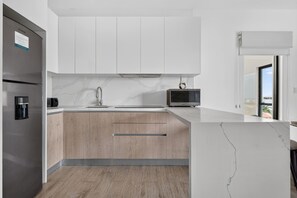 A modern kitchen with a built-in refrigerator, a coffee maker, a microwave, and a sink with a marble backsplash. - Distrito Corazón: Bright 2BR w/ Balcony & Pool (Playa del Carmen)