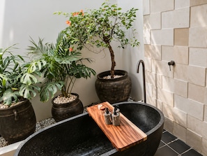 Eine schwarze Badewanne mit einem Holztablett, umgeben von Topfpflanzen und einer Steinmauer.
