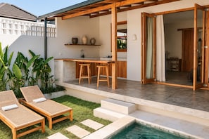 Ein moderner Außenbereich mit Küchenzeile, einer Bar, einem Pool und einer Sitzecke mit Liegestühlen.