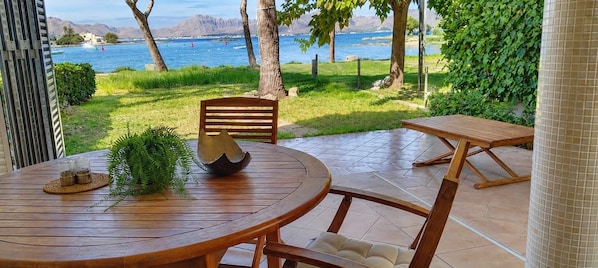 Een houten tafel en stoelen op een terras met uitzicht op een waterpartij en bergen.
