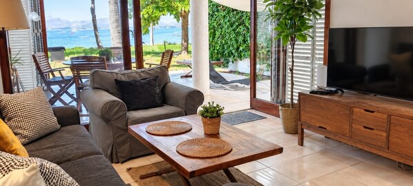 A modern living room with a sofa, a coffee table, and a TV. There is a view of the outdoors through large windows.