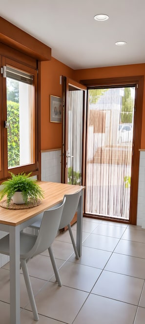 A modern kitchen with a wooden table, grey chairs, and a potted plant.
