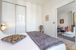 Ett modernt hotellrum med en säng, ett nattduksbord, en lampa, en stol och utsikt över matsalen.