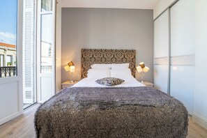 Ett sovrum med en stor säng, två sänglampor, en mönstrad sänggavel och utsikt mot omgivningen.
