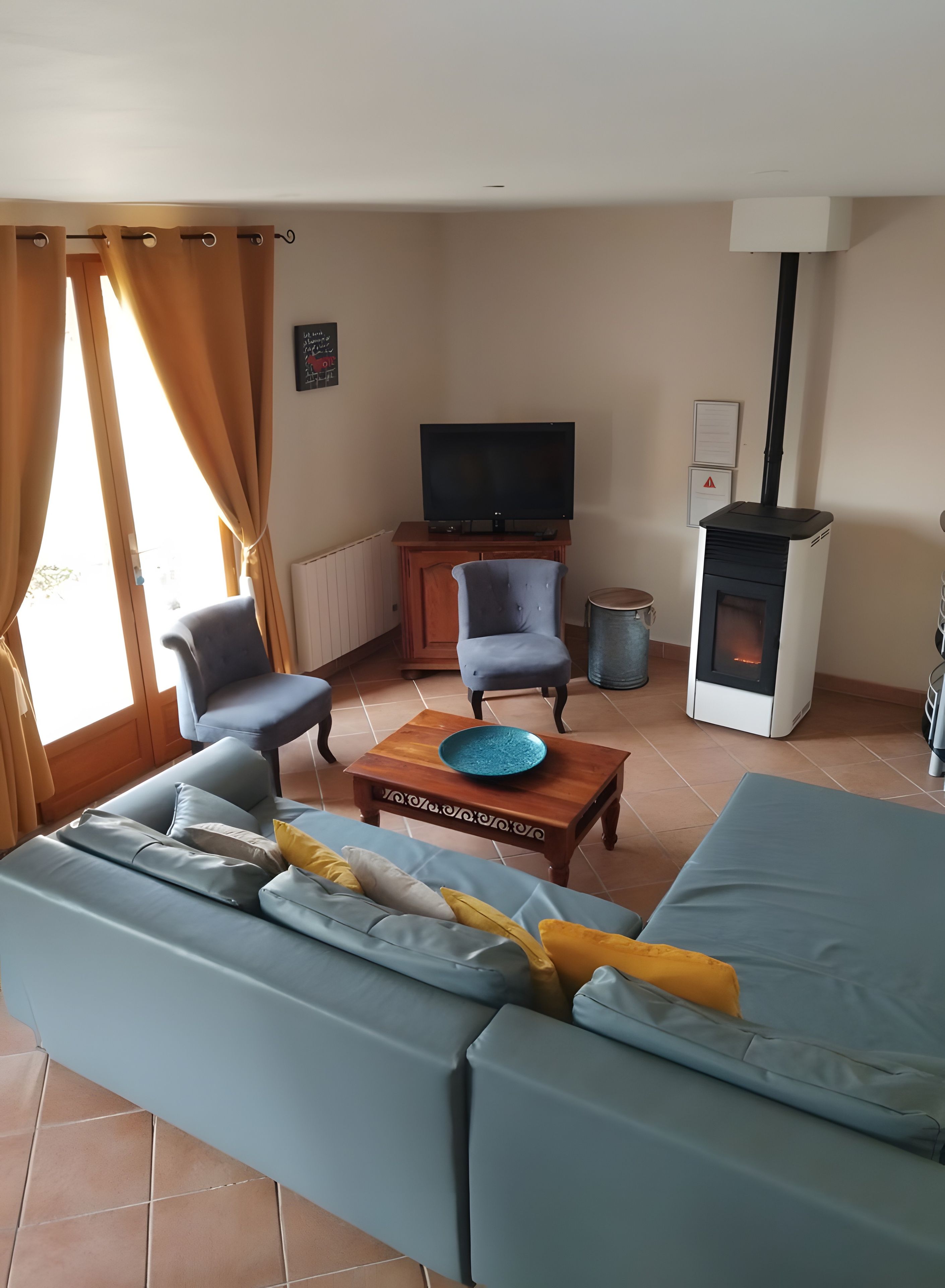 A living room with a sofa, two armchairs, a coffee table, a television, and a wood-burning stove.