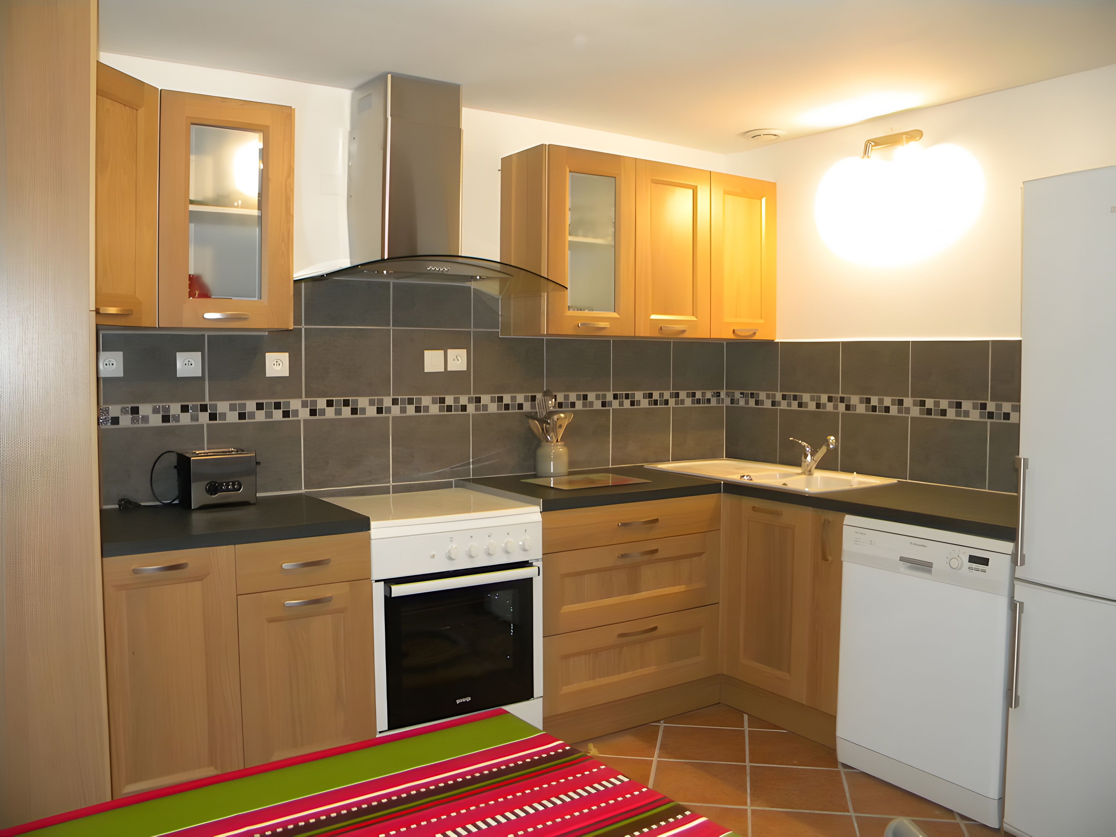 A modern kitchen with wooden cabinets, a built-in oven, a dishwasher, and a tiled backsplash.