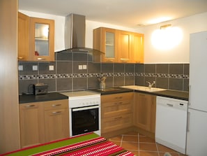 A modern kitchen with wooden cabinets, a built-in oven, a dishwasher, and a tiled backsplash.