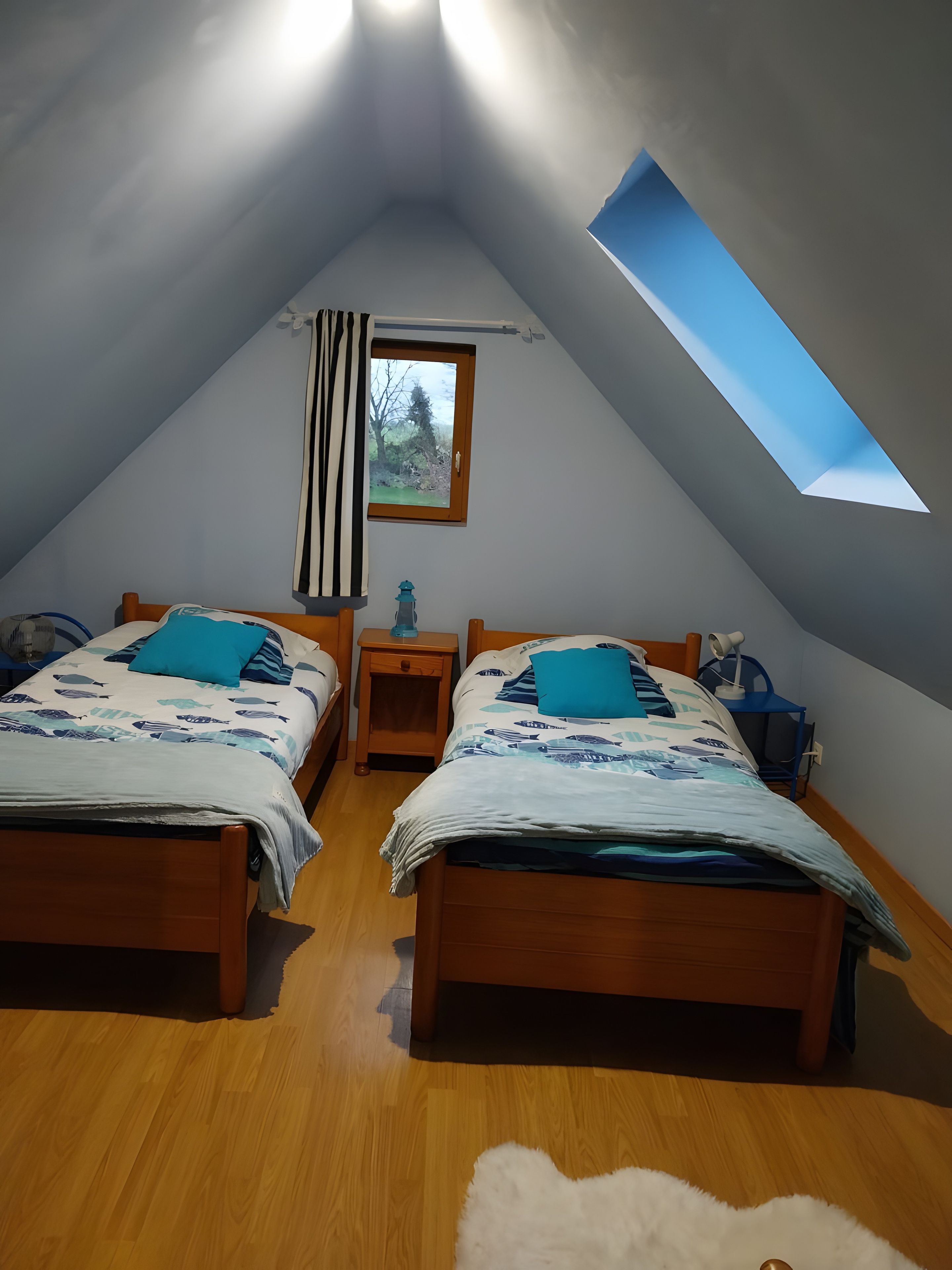 Une chambre avec deux lits, une lucarne, une fenêtre et une table de chevet.