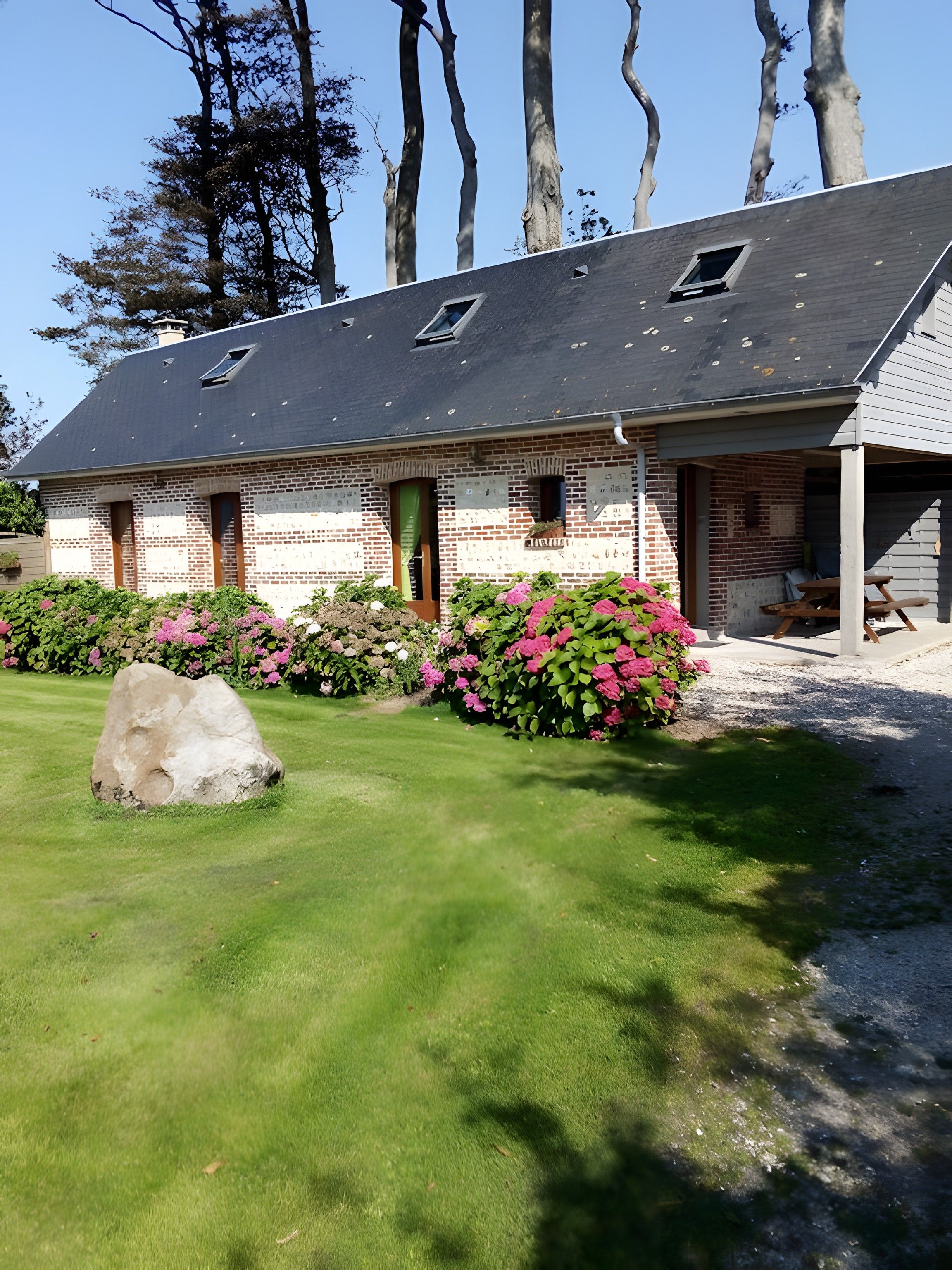 Un bâtiment en briques avec un toit en pente, une petite fenêtre et une pierre au premier plan.