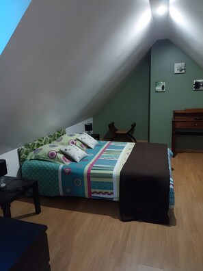 A bedroom with a sloped ceiling, a bed with patterned bedding, a desk, and a chair.