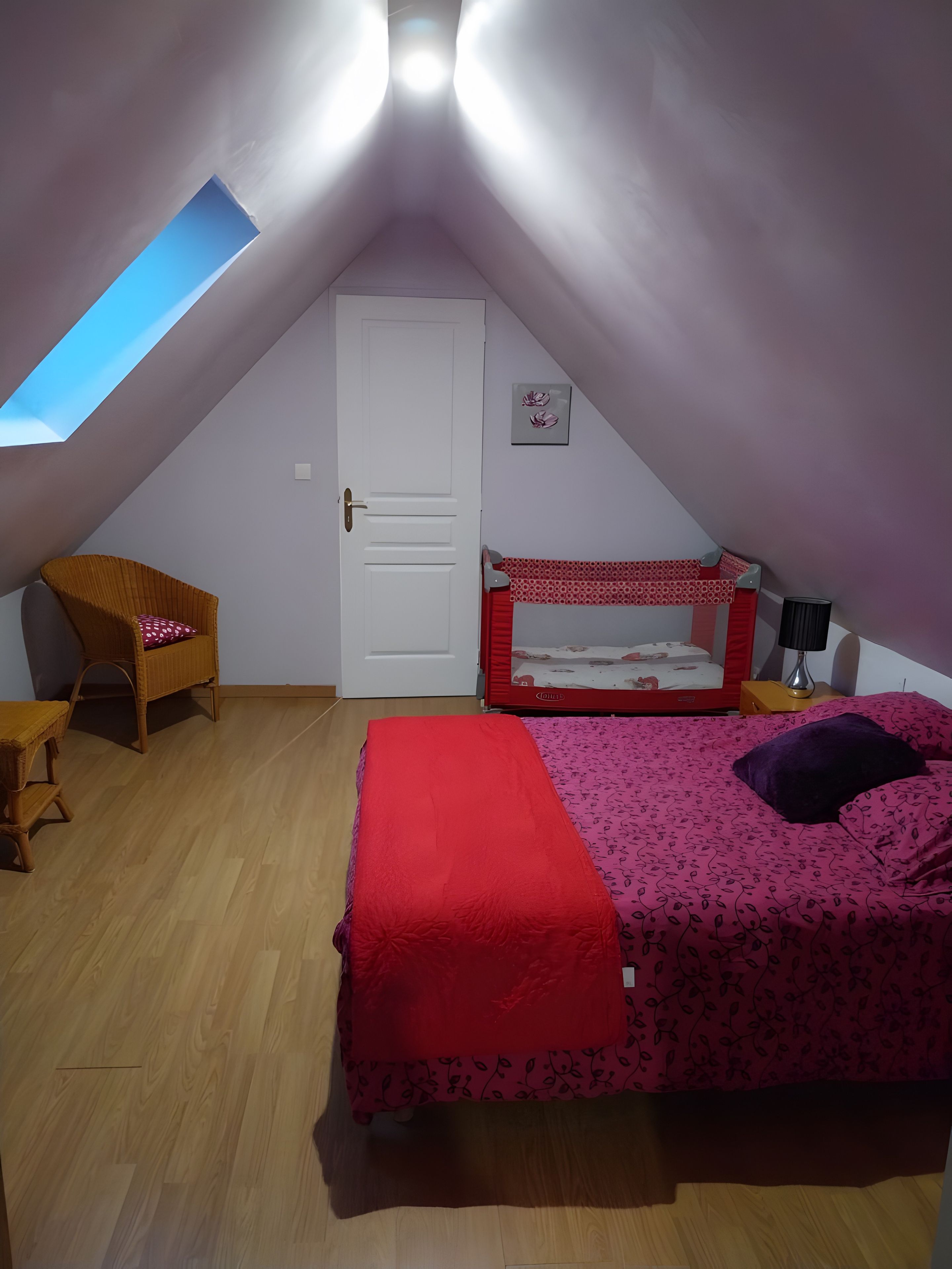 Une pièce avec un plafond en pente, un lit superposé, une chaise, une table de chevet et une petite fenêtre.