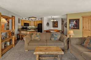 A cozy living room with a wooden sofa, a coffee table, and a kitchen area with wooden cabinets and a microwave. - Walk to Lifts, Main St! (Breckenridge)