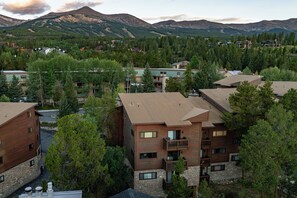 A multi-story building with a stone facade and a balcony, surrounded by dense forest and mountains in the background. - Walk to Lifts, Main St! (Breckenridge)