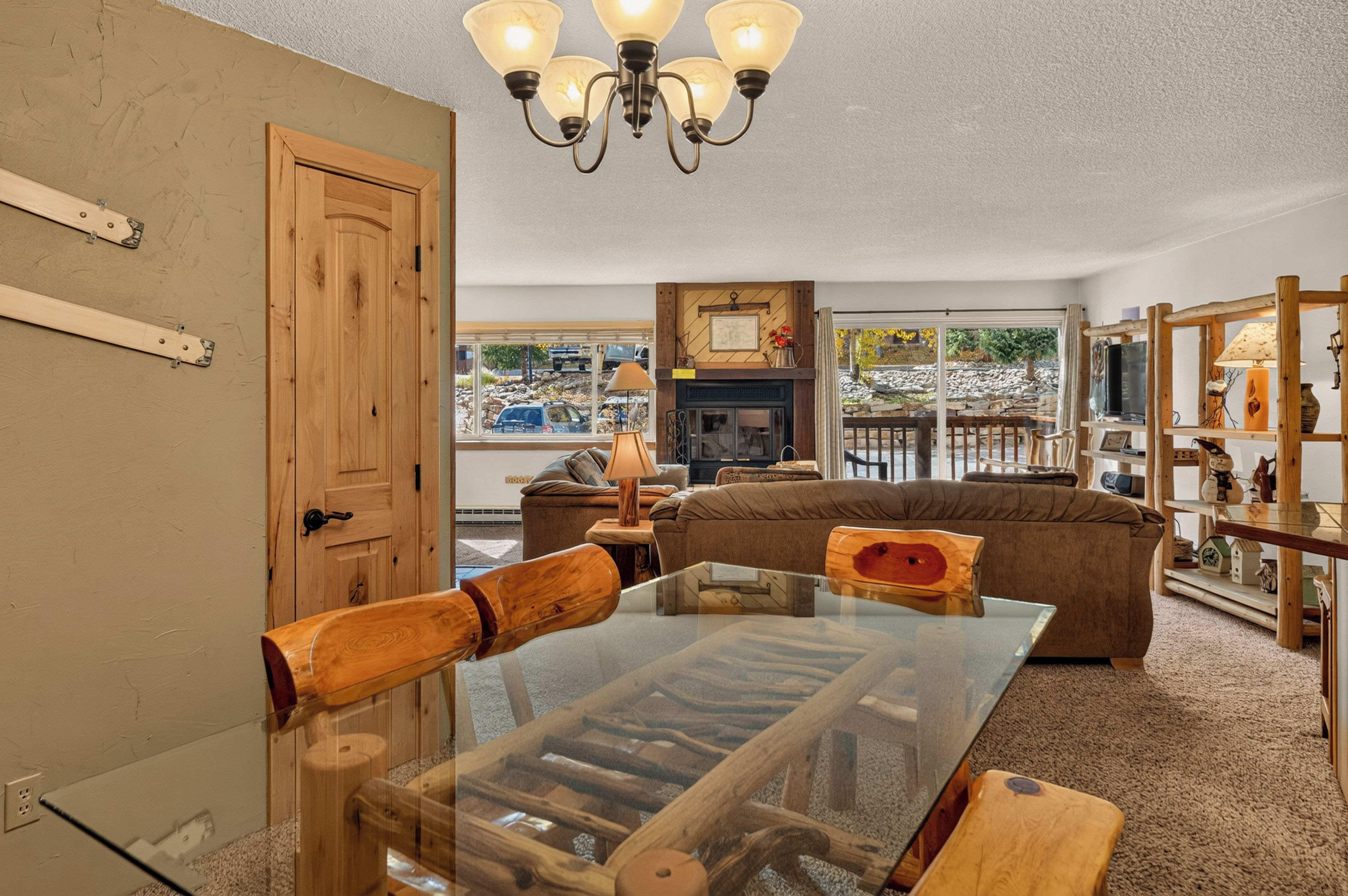 A cozy living room with a glass-top coffee table, wooden chairs, a brown sofa, and a fireplace.
