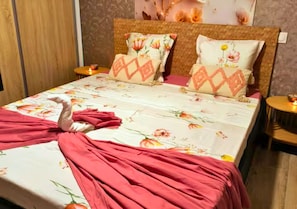 Ein Bett mit blumigem Bettbezug, zwei Kissen mit floralem Muster und ein rotes Tuch auf dem Bett.