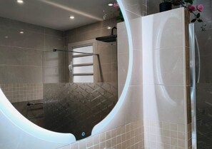 Une salle de bain moderne avec un miroir incurvé, une baignoire et un espace douche.