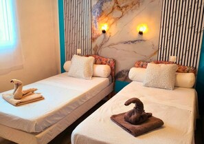 Deux lits jumeaux avec des serviettes décoratives, un mur en marbre et des lampes fixées au mur.